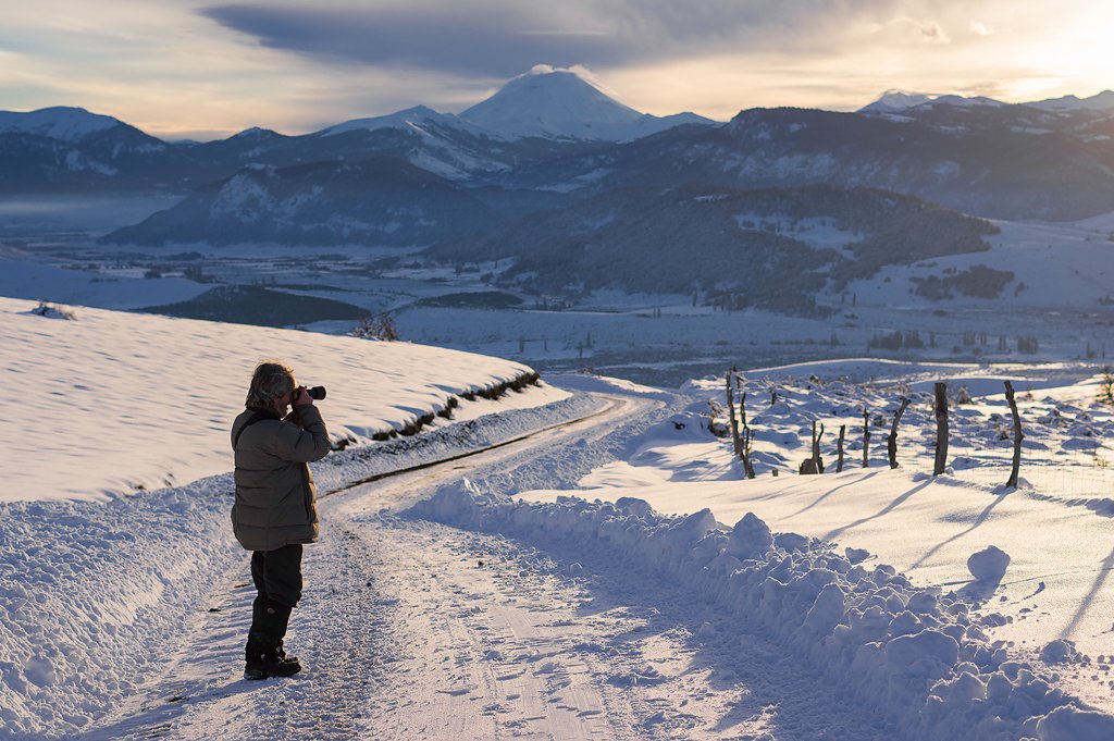 Fotógrafo observando paisaje cordillerano nevado al atardecer